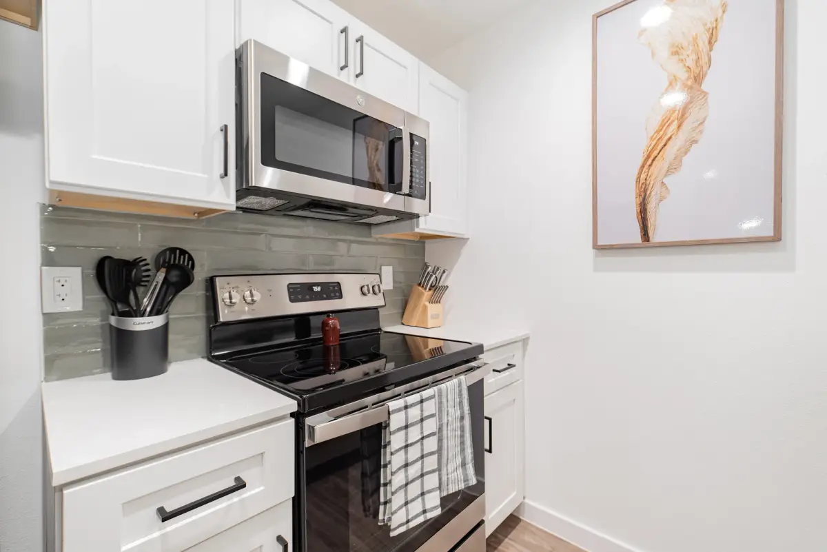 Galley kitchen with white shaker cabinets, white quartz counters, a stainless range and microwave, and a gray subway-tile backsplash