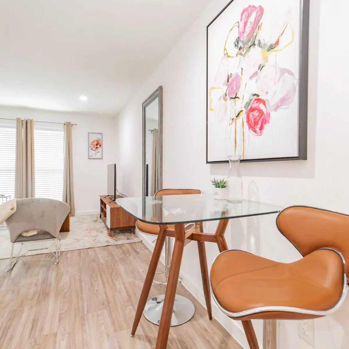 Dining and living area with a glass table and chairs, floral artwork, and a leaning mirror