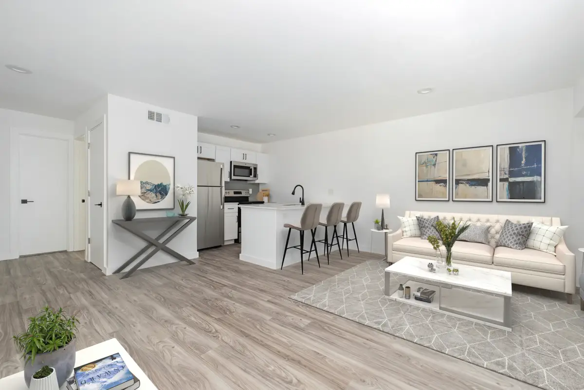 Open living and kitchen area with a sofa, kitchen island with bar stools, and framed wall art