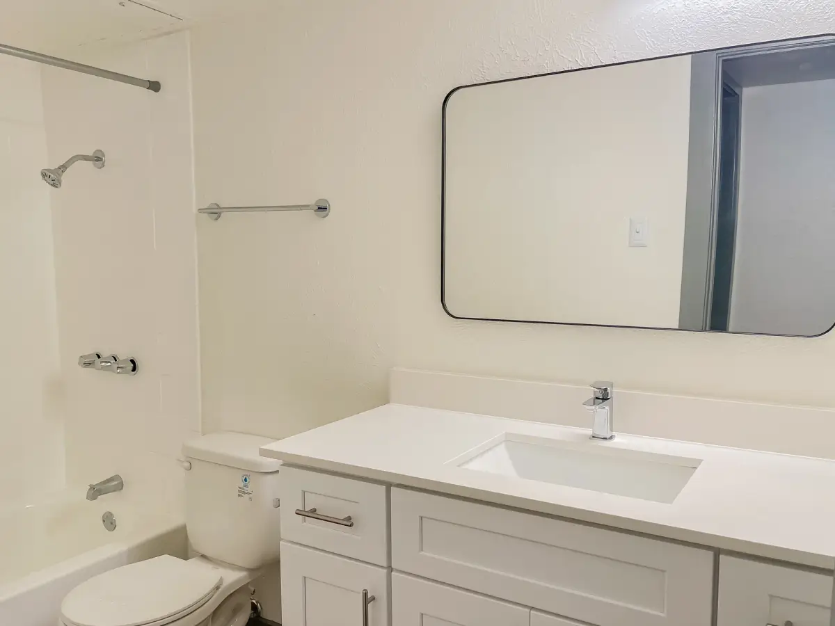 Bathroom with a white vanity, white vanity top, a framed mirror, chrome fixtures, and a white tub-and-shower