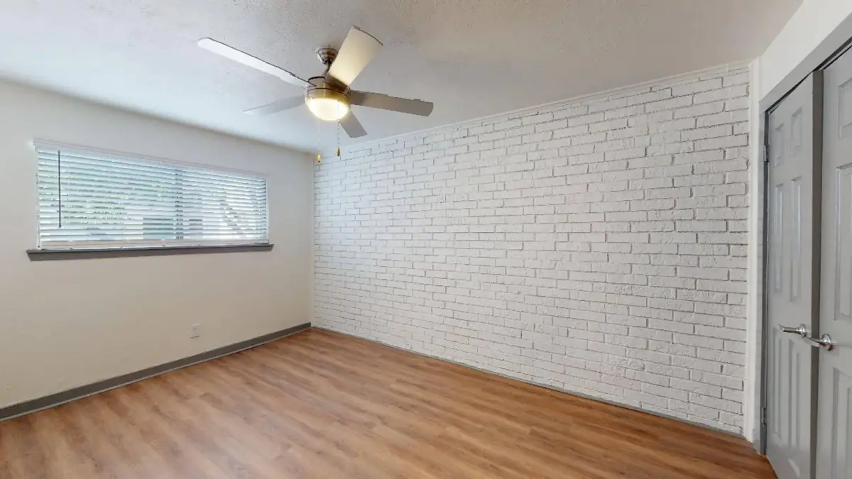 Bedroom with a white-painted brick accent wall, a ceiling fan, and a blinded window