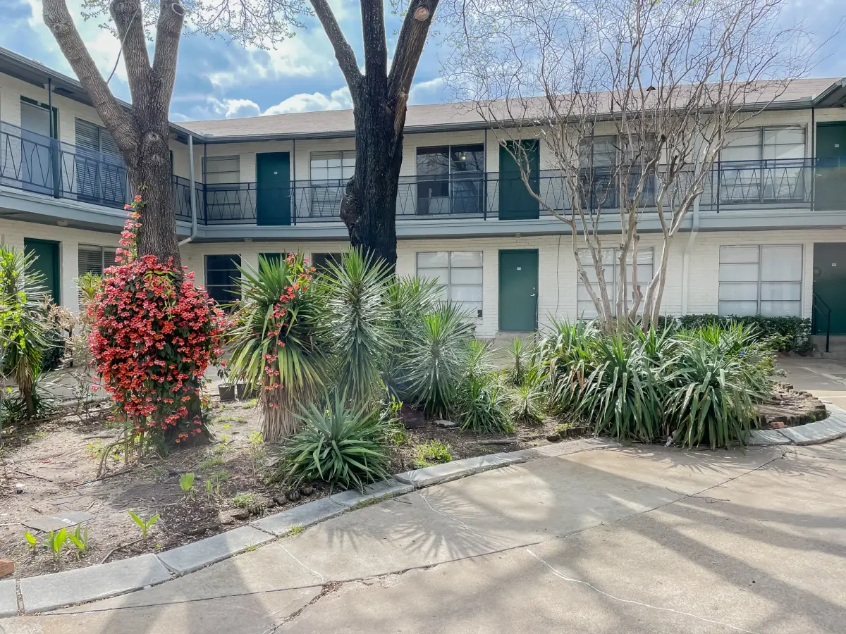 Interior courtyard framed by two-story buildings with green doors, mature trees, and agave and yucca plantings