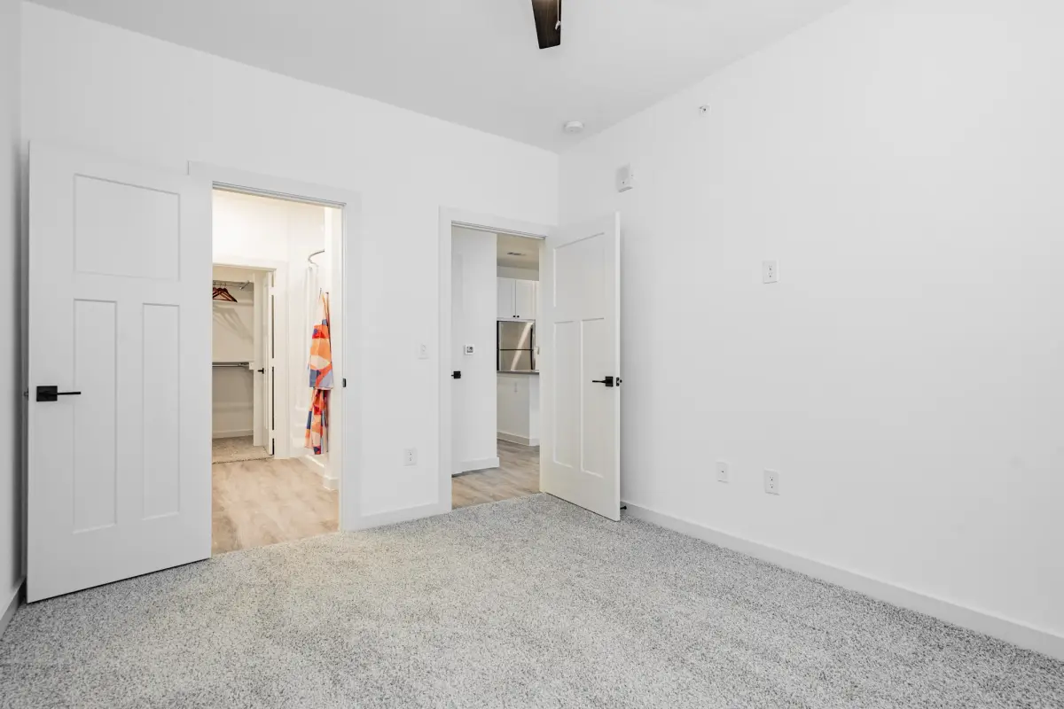 Carpeted bedroom, its matte black levered doors open to the walk-in closet and the hall toward the kitchen