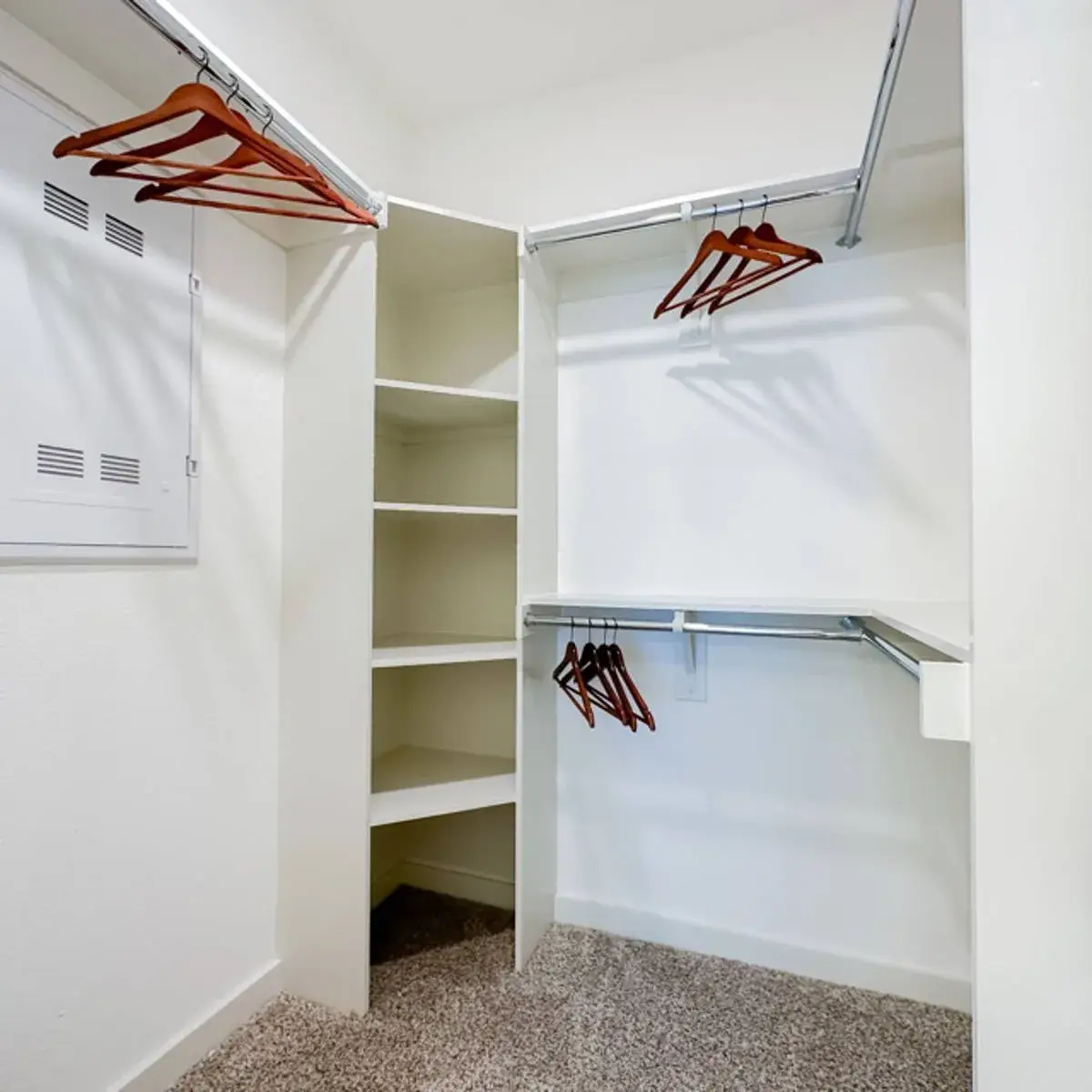 Walk-in closet with wraparound chrome rods, a corner shelf tower and wood hangers over speckled carpet