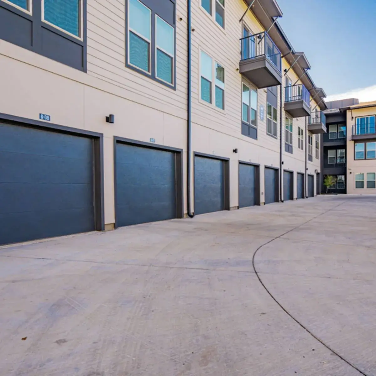 Row of private garages with charcoal doors lining the cream lap-siding building beneath balconies