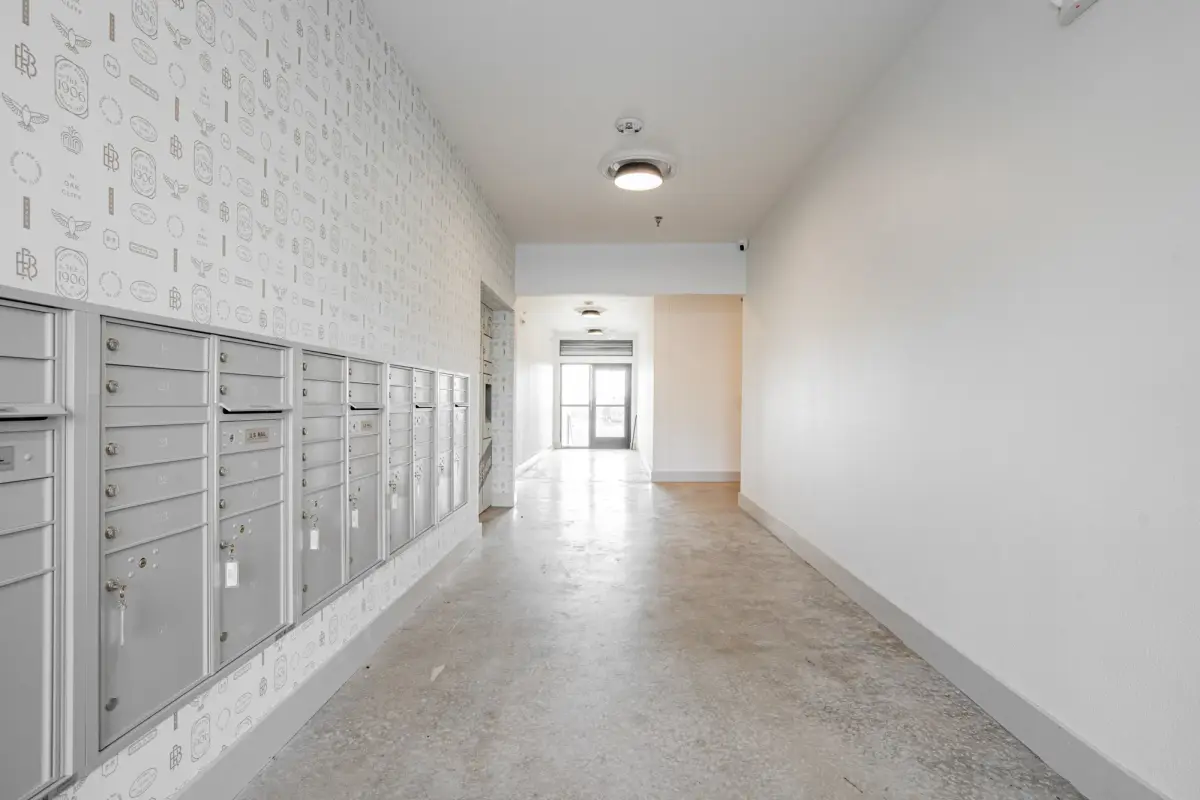 Mail corridor with banks of silver mailboxes under crest-patterned wallpaper and a polished concrete floor