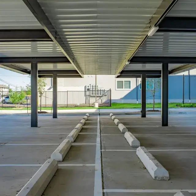 Beneath the carport, a corrugated metal canopy on steel columns shades rows of striped spaces with wheel stops