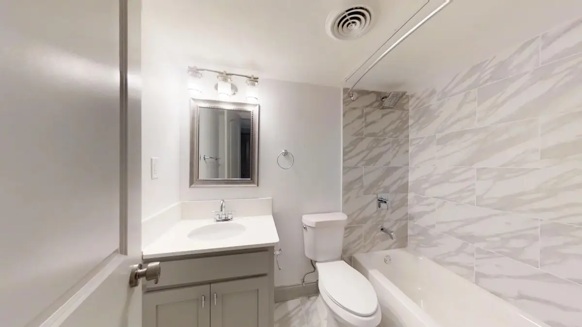 Bathroom with a white vanity, framed mirror, and a marble-look tiled tub-and-shower surround