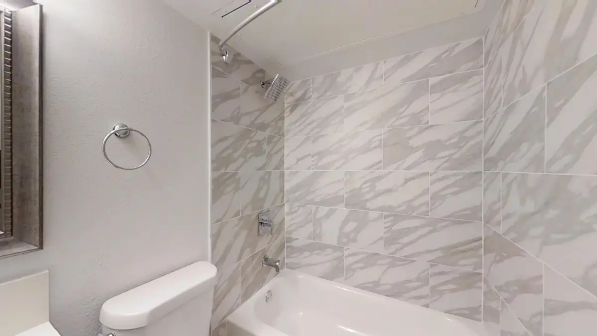 Bathroom with a marble-look tiled tub and shower beside the toilet