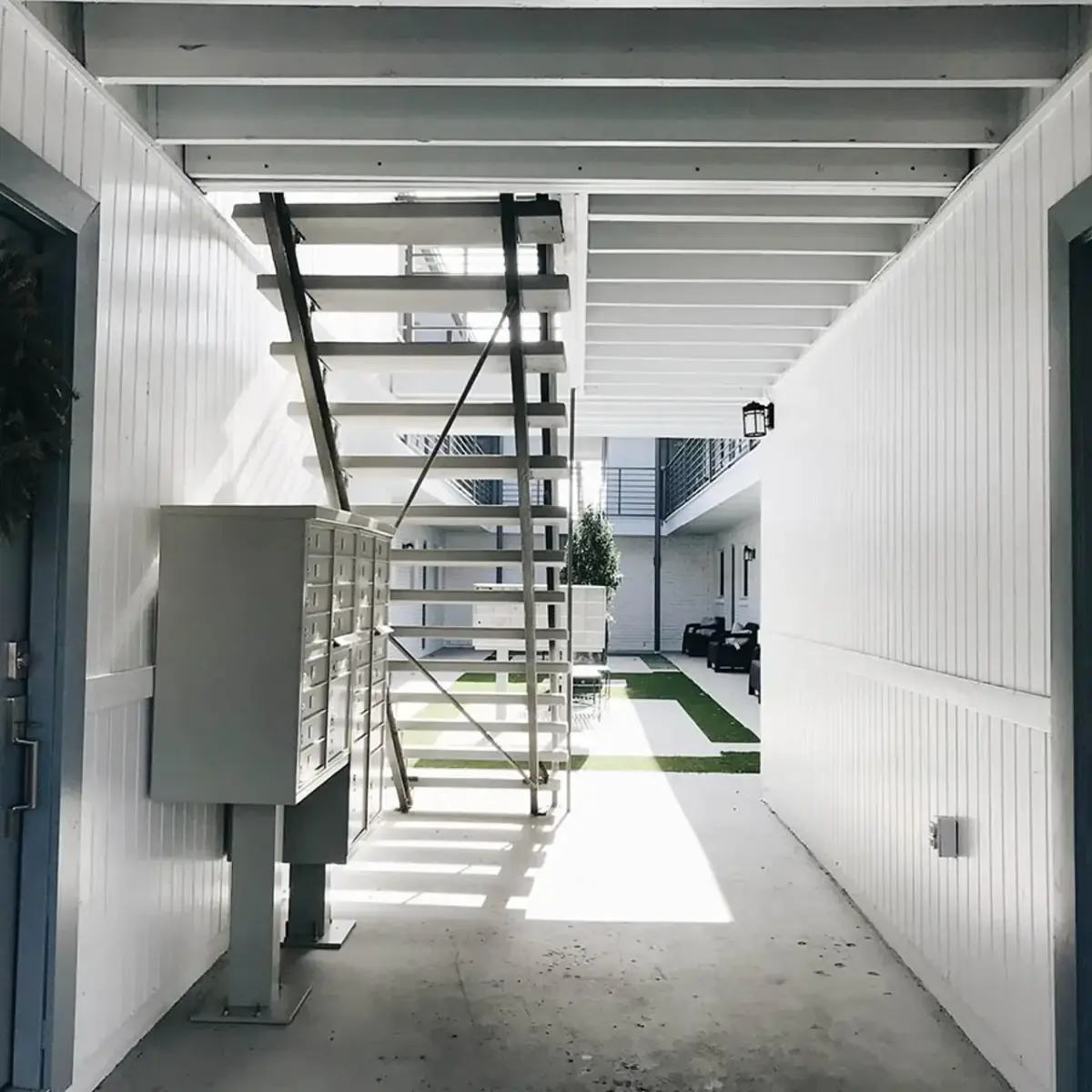 Covered breezeway with cluster mailboxes and an open-tread staircase opening onto the courtyard