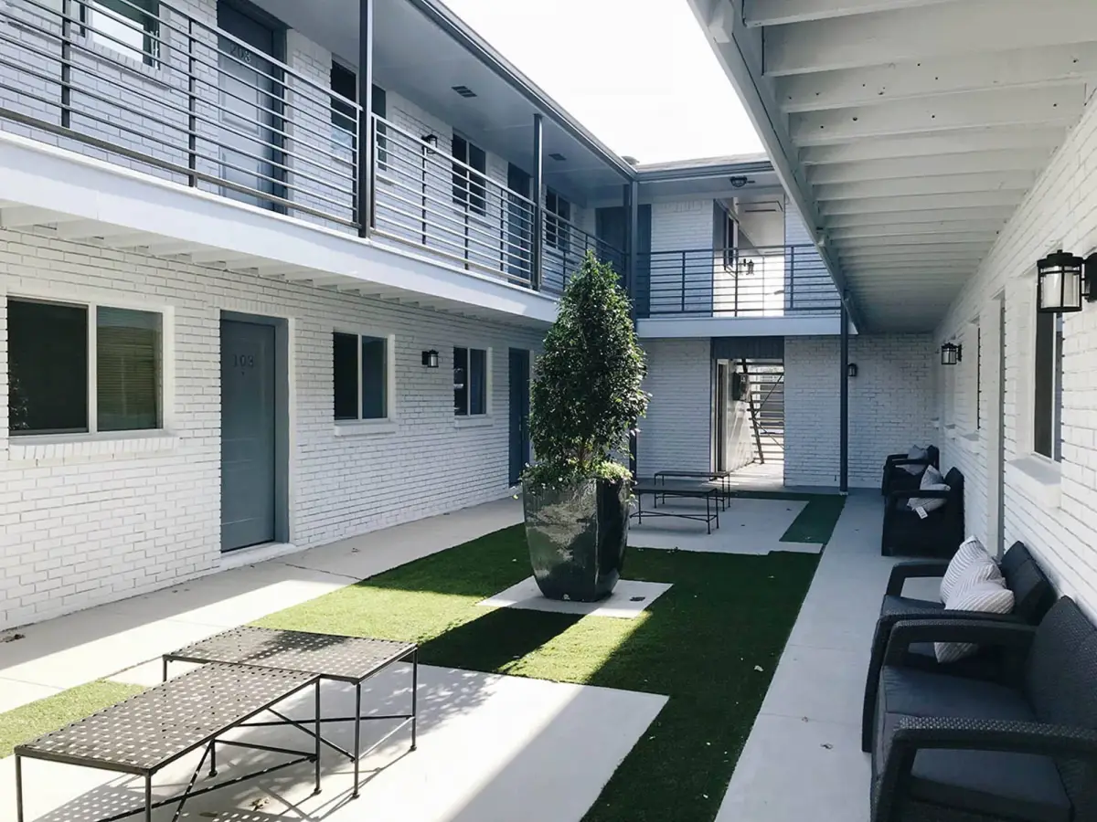 Landscaped courtyard with a central potted tree, turf strips, and patio seating framed by the two-story building