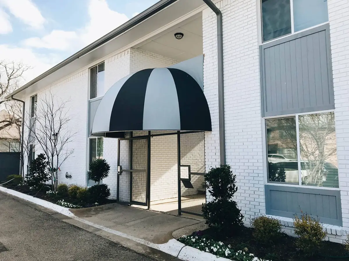 Entrance to The Apollo with a black-and-white domed awning over a glass door, set in white-painted brick