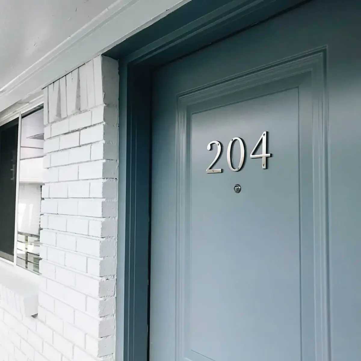 A gray apartment entry door numbered 204 framed by painted white brick