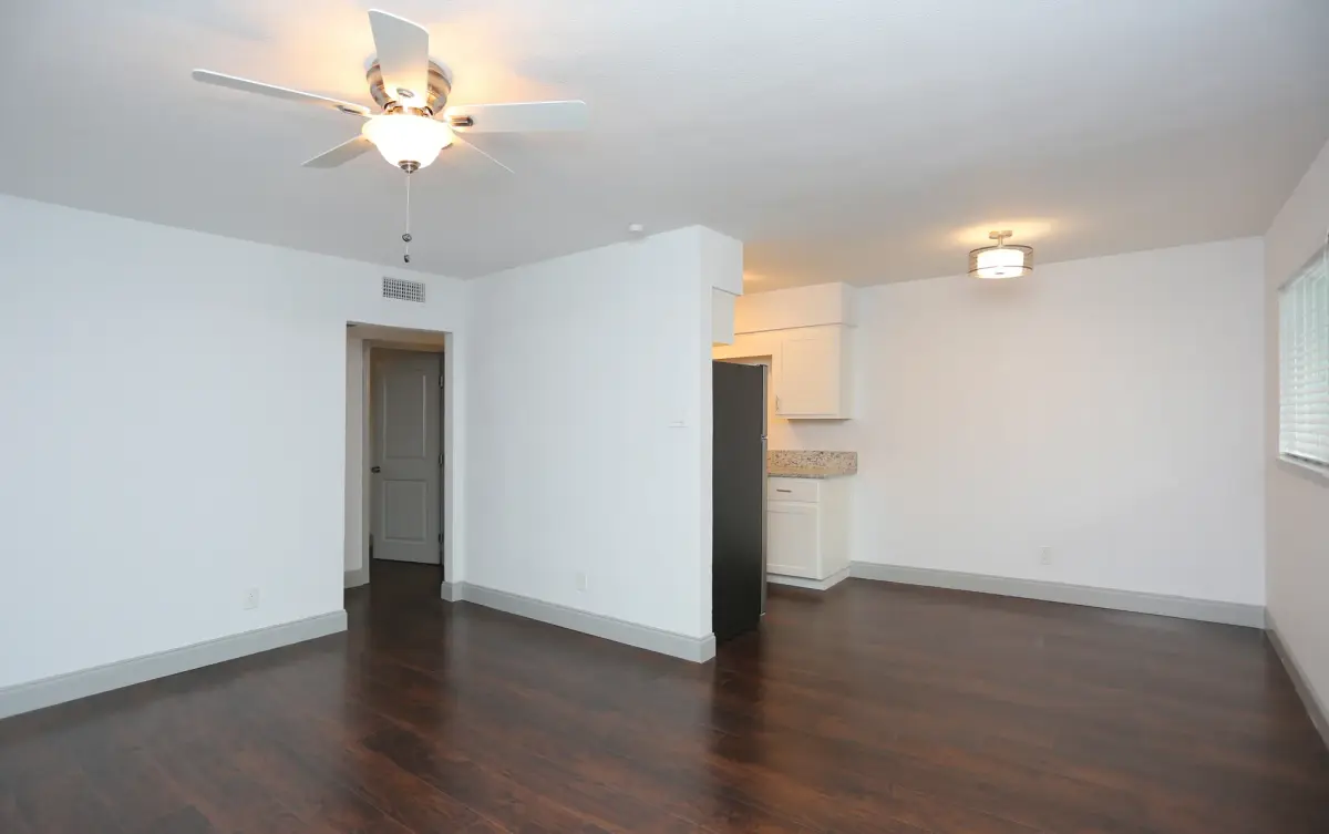 Living room with wood-look flooring opening to a hallway and the kitchen