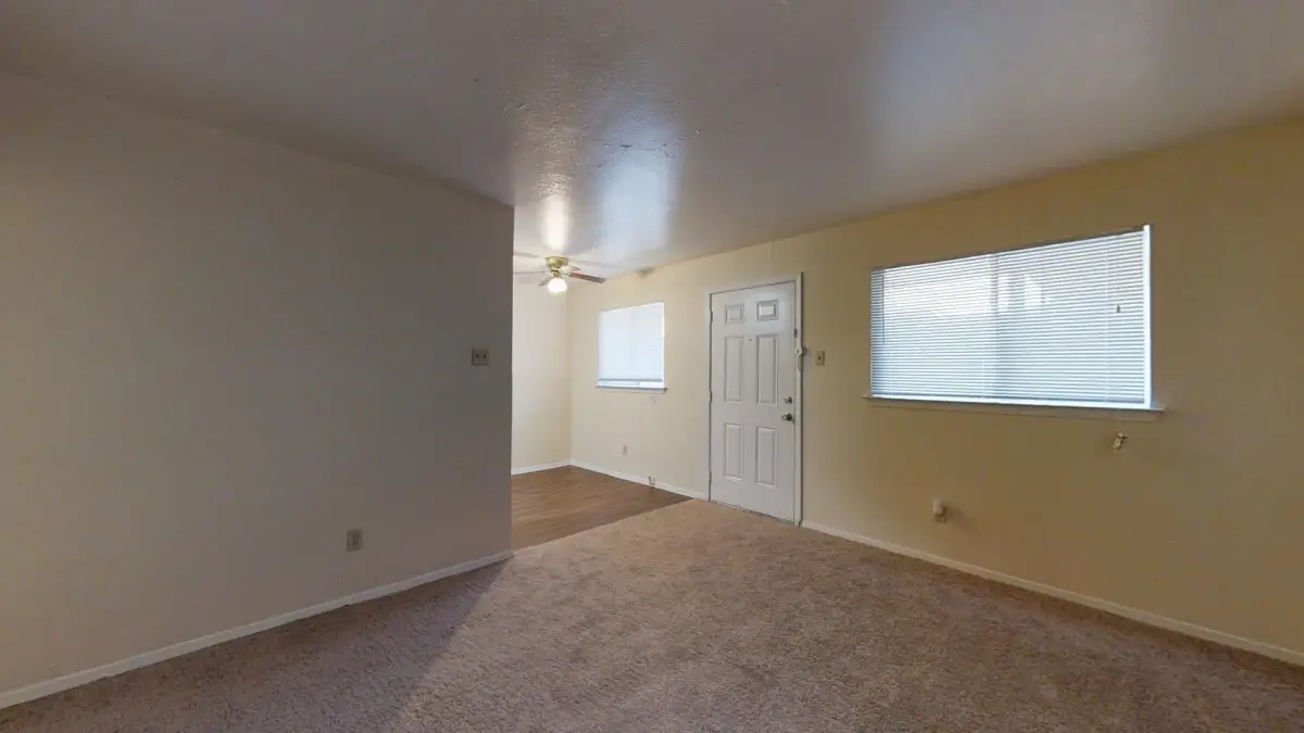 Carpeted living room with beige walls, a ceiling fan, and an entry door flanked by windows