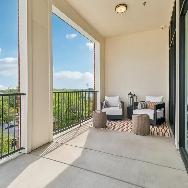 Covered balcony with two cushioned lounge chairs, a geometric rug, and wicker side tables above the treetops