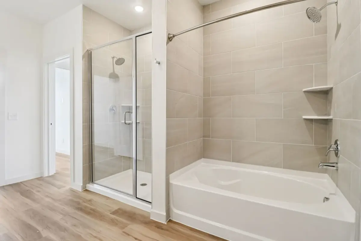 Glass-door shower beside a soaking tub with beige large-format tile surround and corner shelves