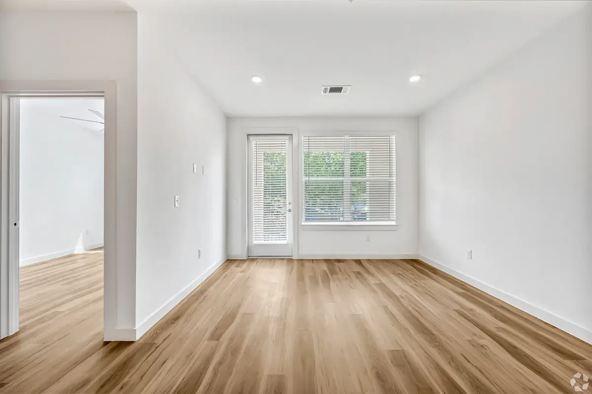 Unfurnished bedroom with a glass patio door and wide blinds-covered window overlooking greenery