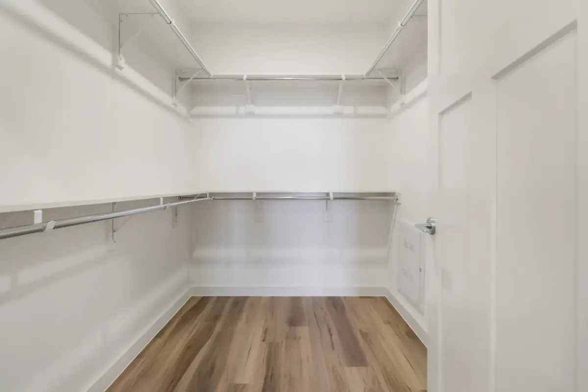 Walk-in closet with double-hang chrome rods, a full white shelf run, and wood-look plank flooring