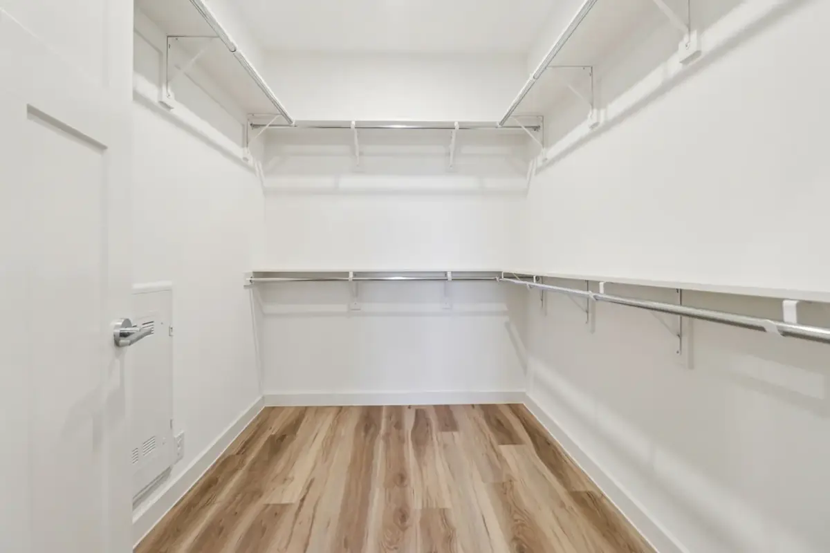 Long walk-in closet with wraparound white shelving, chrome hanging rails, and light plank flooring