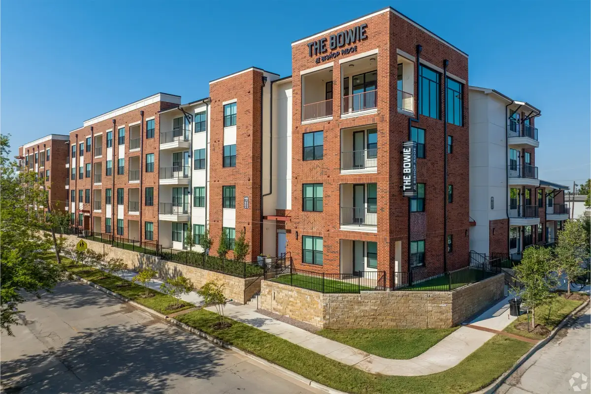 Red-brick and white four-story exterior of The Bowie with painted corner signage, balconies, and stone garden walls