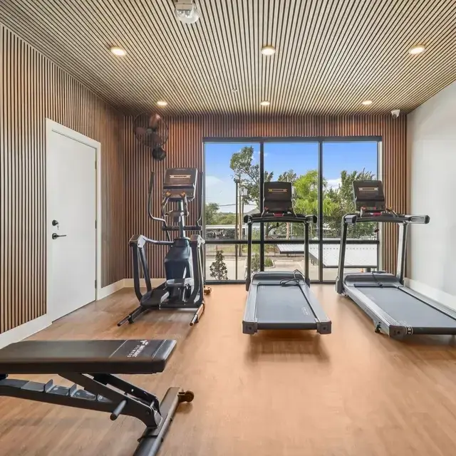 Wood-slat fitness room with treadmills, an elliptical, and a weight bench facing a full-height window
