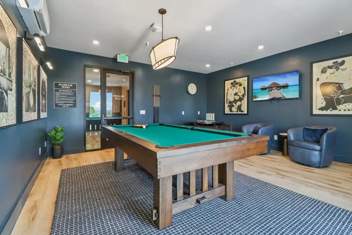 Billiards room with navy walls, green-felt wood pool table, drum pendant, leather chairs, and wall-mounted TV