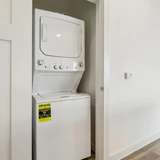 White stacked washer-dryer laundry center in a dedicated closet with wood-look flooring