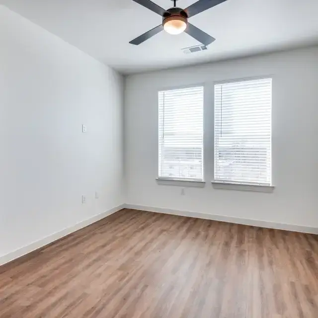 Bedroom with two windows, a dark-blade ceiling fan, and wood-look flooring