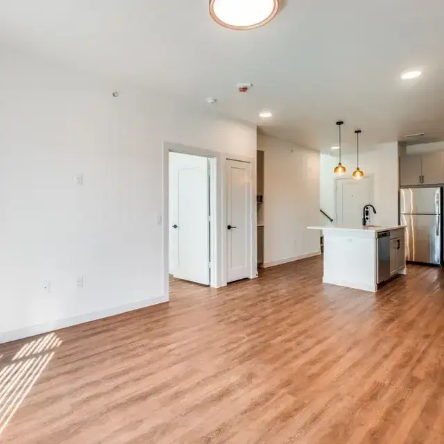 Living space with wood-look flooring, recessed and pendant lighting, and the kitchen beyond