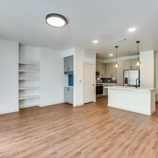 Living area with built-in floating shelves and a gray cabinet nook adjacent to the kitchen