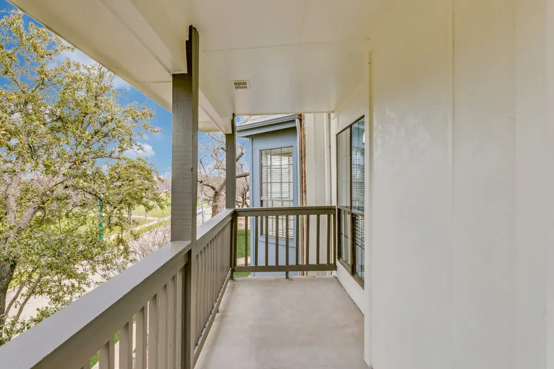 Private covered balcony with a wood railing and a tree-lined street view