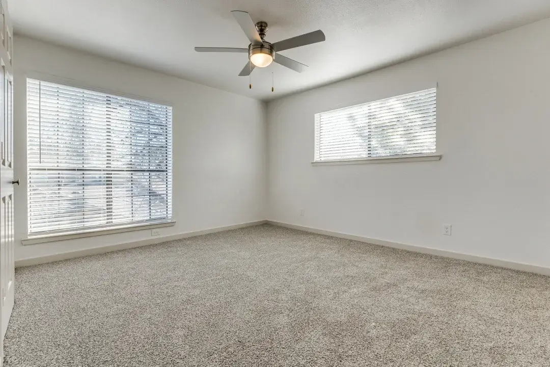 Empty carpeted bedroom with a ceiling fan and two blinded windows