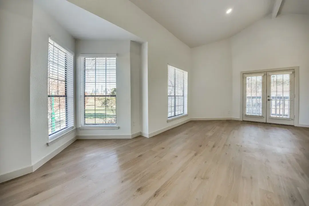 Empty living room with a vaulted ceiling, a bay window, and French doors to the balcony
