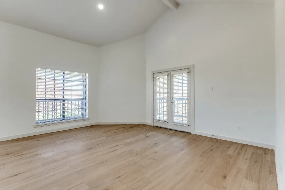 Empty living room with a vaulted ceiling and French doors opening to a balcony
