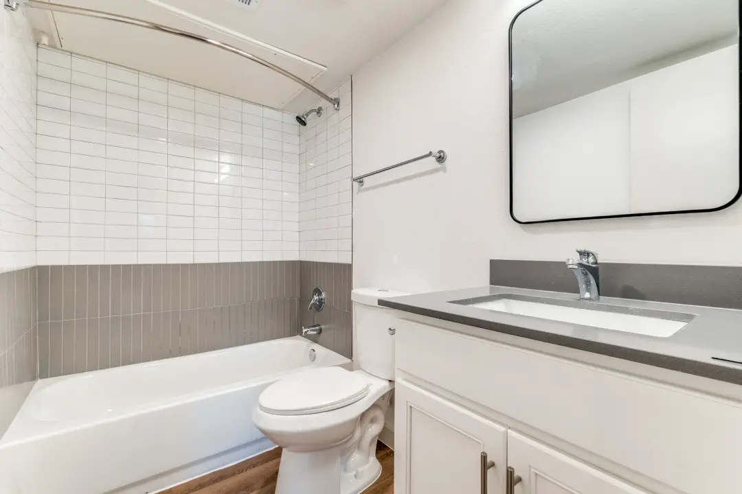 Bathroom with a white vanity, gray quartz top, a black-framed mirror, and a white-and-gray subway-tile tub-and-shower