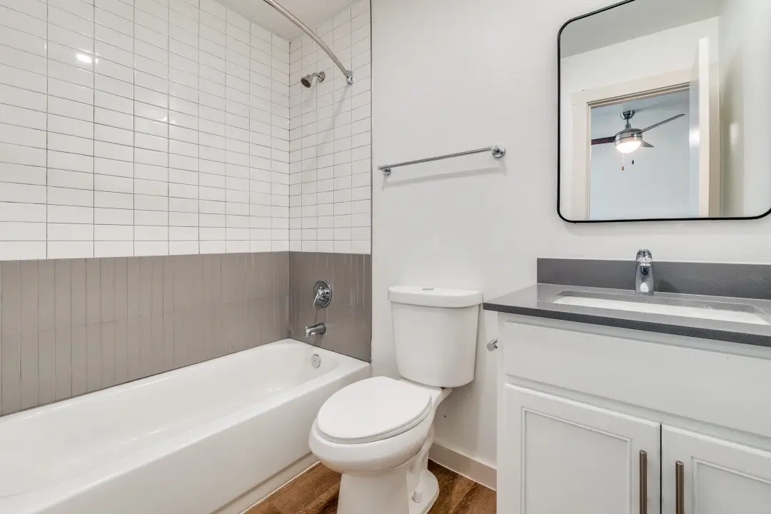 Bathroom with a white vanity, gray quartz, a black-framed mirror, and a white-and-gray subway-tile tub-and-shower