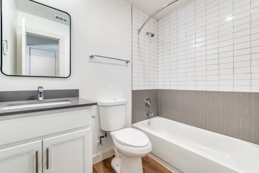 Bathroom with a white vanity, gray quartz, chrome fixtures, and a white-and-gray subway-tile tub-and-shower