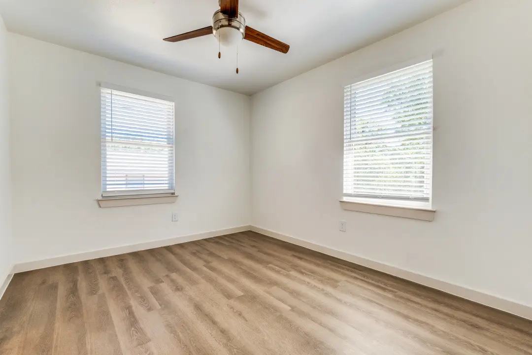 Empty bedroom with a wood-blade ceiling fan, two blinded windows, and wood-look flooring