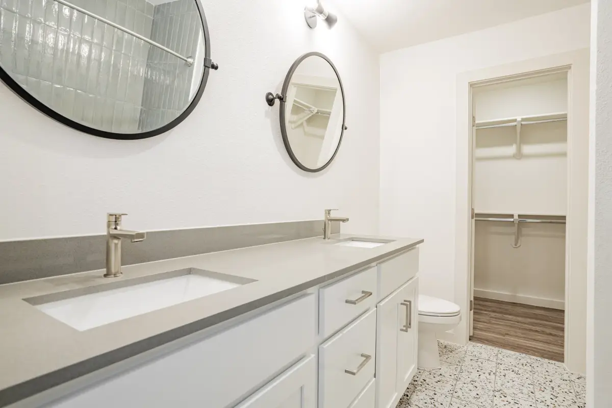 Bathroom with a white double-sink vanity, quartz top, two round black mirrors, and an adjoining walk-in closet