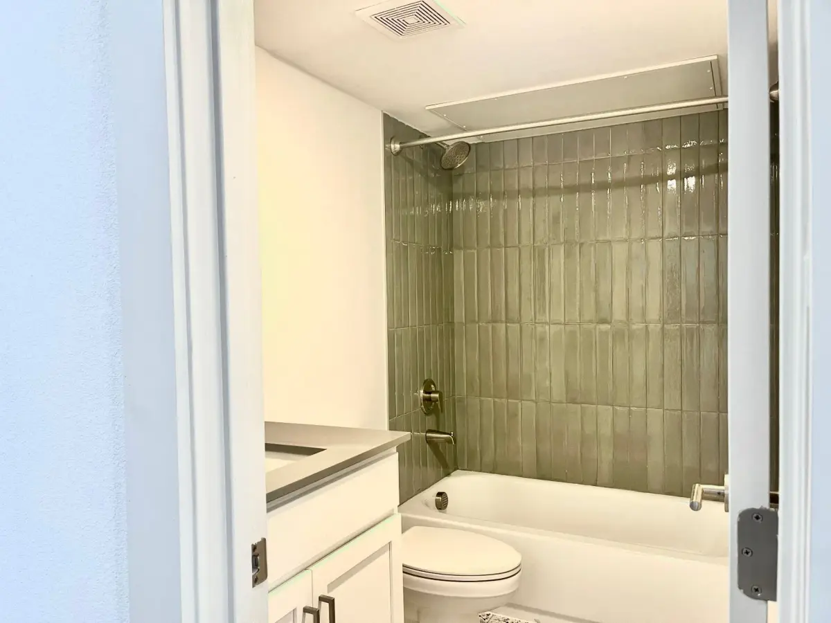 Bathroom with a white vanity, quartz top, and a sage-green tiled tub-and-shower