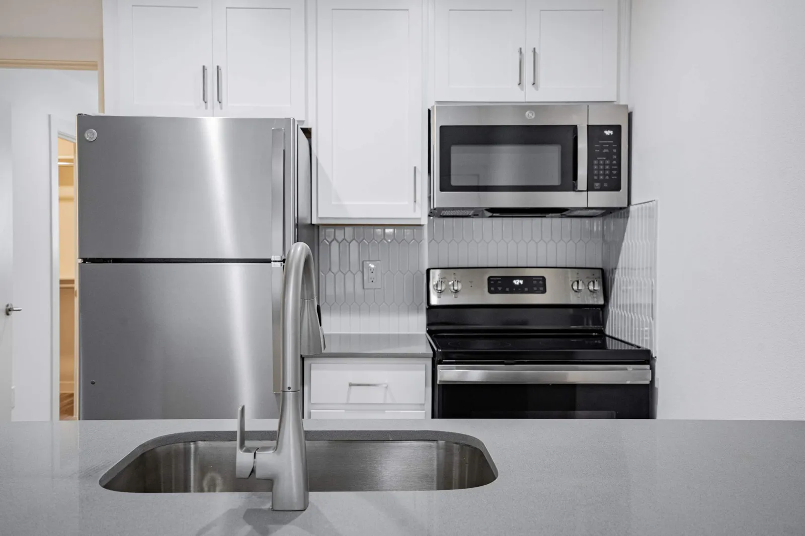 Kitchen with a stainless refrigerator, range and microwave against a white picket-tile backsplash and quartz counters