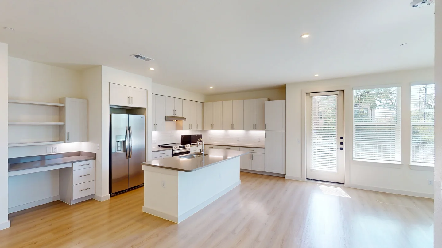 Inside a finished three bedroom at The Parker: kitchen island, built-in desk and corner windows width=