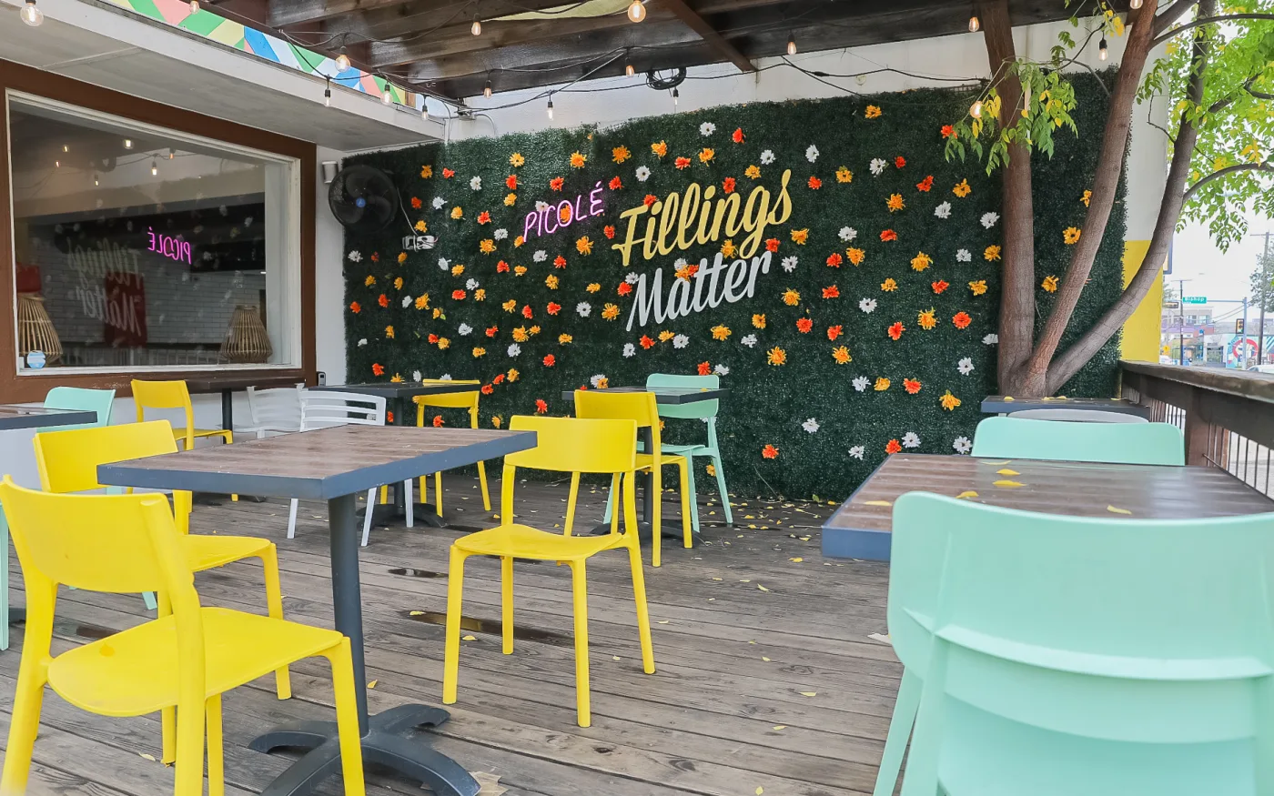 The flower-wall patio at a Bishop Arts District popsicle shop, with bright chairs under string lights